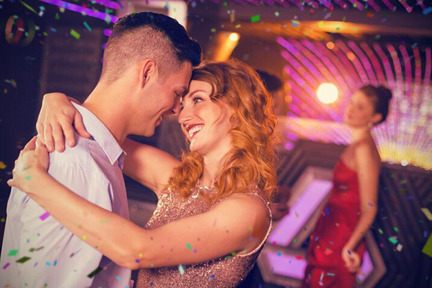 Casal sorridente dançando em festa liberal com luzes e clima descontraído