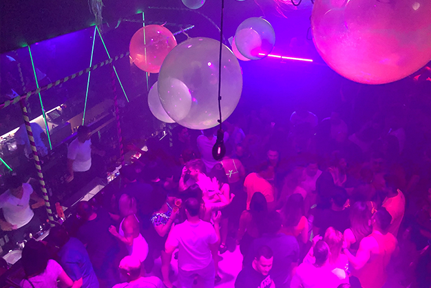 Ambiente de festa liberal com iluminação vermelha e casais interagindo de forma respeitosa